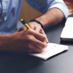 writing notes on a piece of paper beside laptop