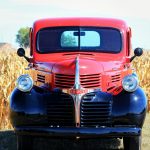 red, vintage Dodge pickup truck sitting in front of a cornfield