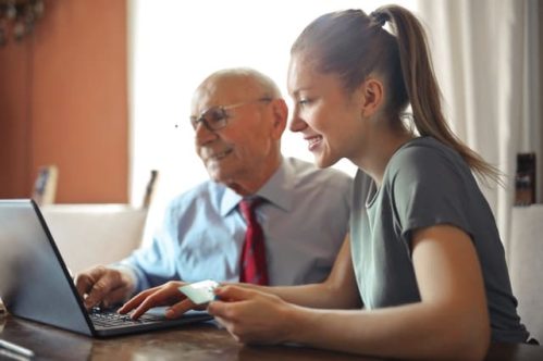 an old man and a young lady in front of laptop