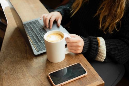 long-haired person holding a mug while scrolling through laptop