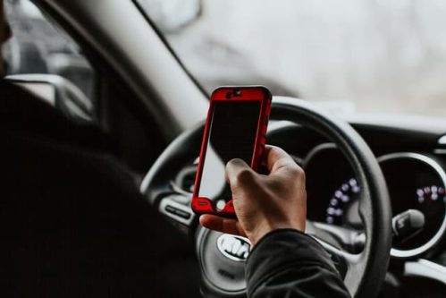 person holding phone in red casing while in front of steering wheel