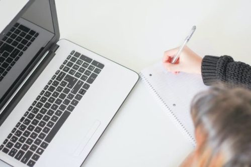 person in front of laptop while writing on a notebook
