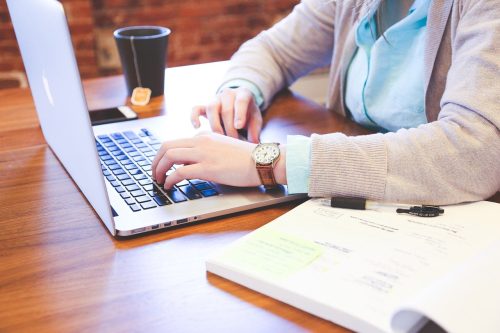 person using laptop with tea and notebook on the side