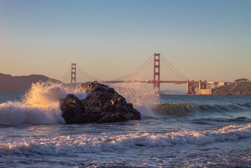 waves crashing against rock with the Golden Gate Bridge as background