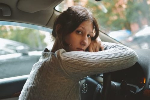 woman in brown sweater resting head on steering wheel