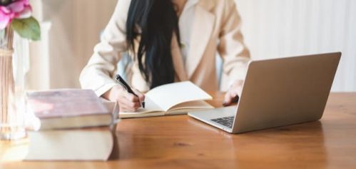 woman writing on notebook while using laptop