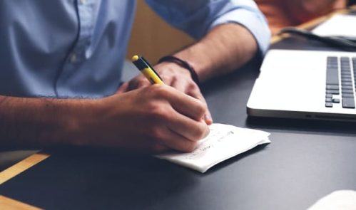 writing notes on a piece of paper beside laptop